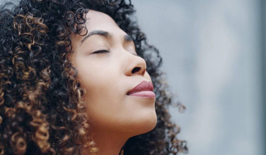 an individual with curly hair facing up with closed eyes trying emotional regulation