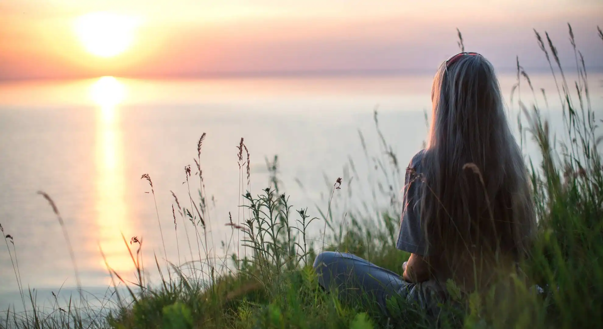 woman sitting in front of a lake where sun is setting
