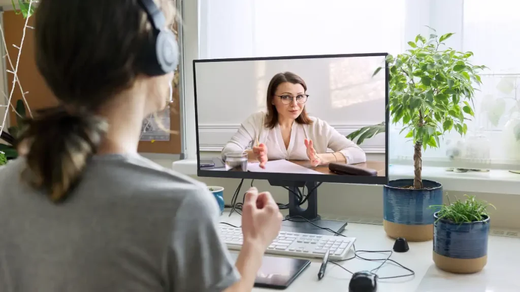 a person sitting at a desk with headphones on while talking to a therapist on a computer screen.