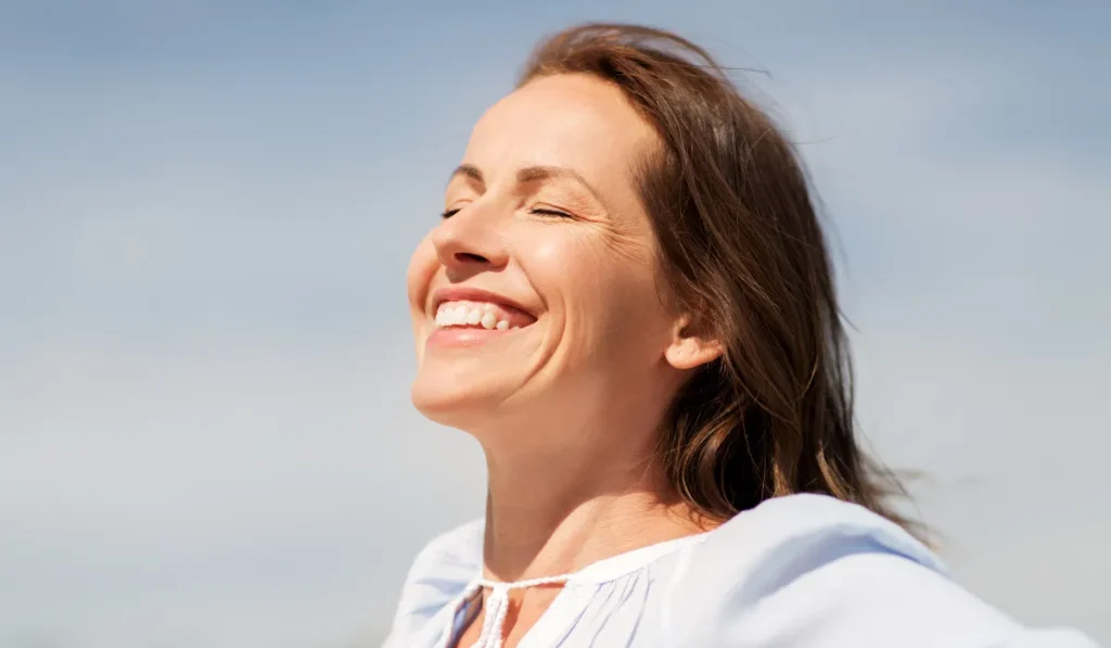 Woman smiling peacefully outdoors with her eyes closed in natural light.