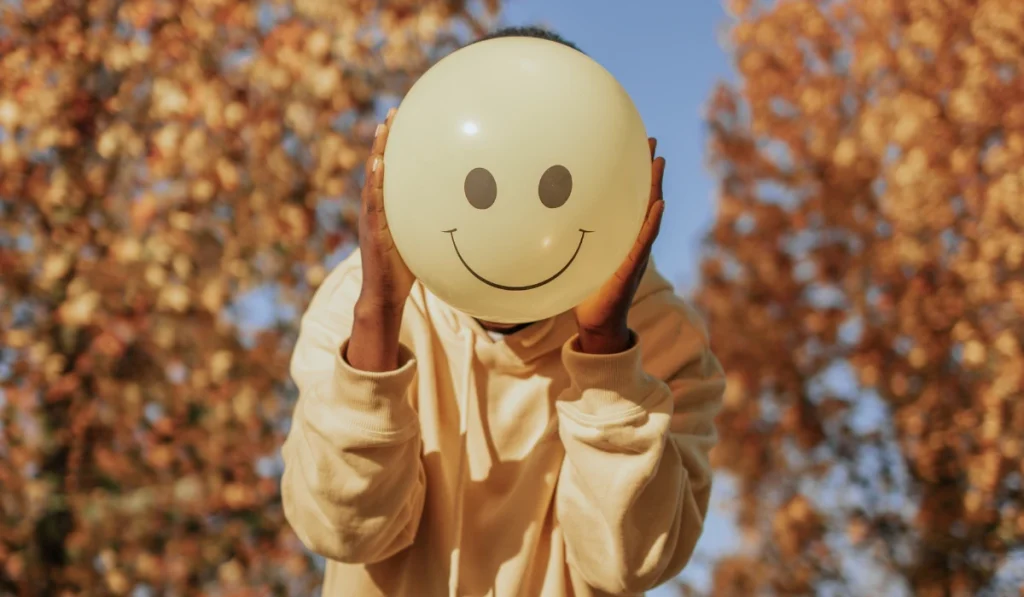 Person holding a smiley face balloon outdoor.