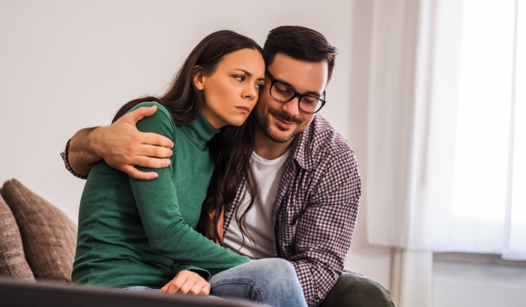 Couple sitting together on a couch as one partner offers comfort